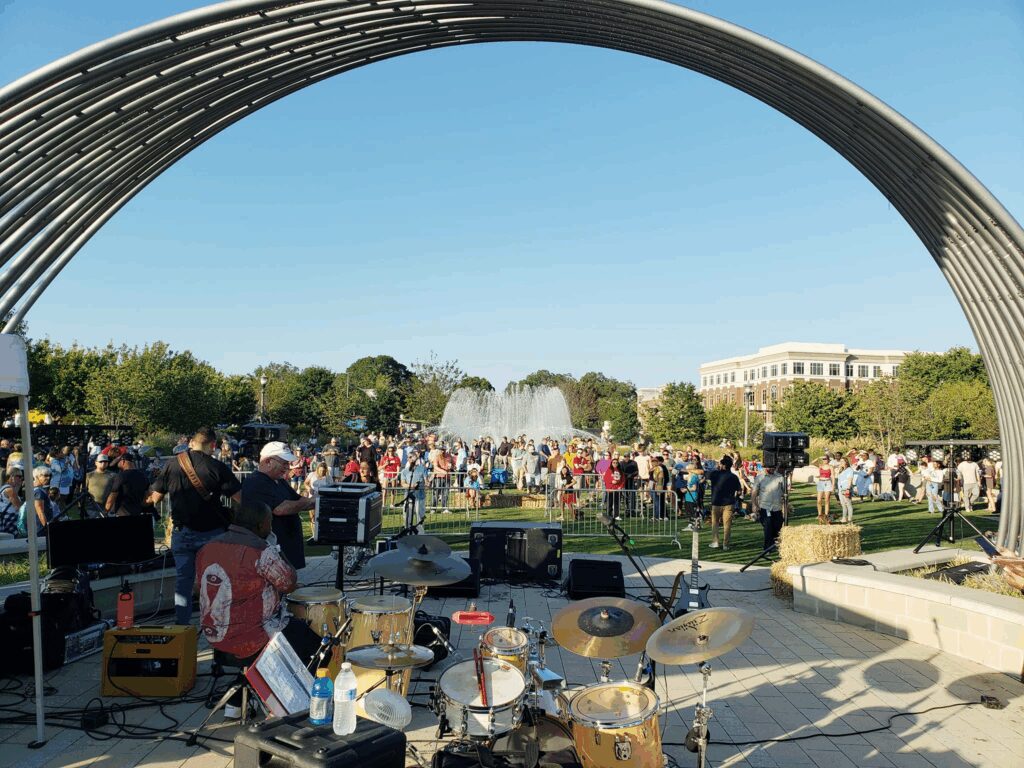 Outdoor concert with crowd and fountain backdrop.