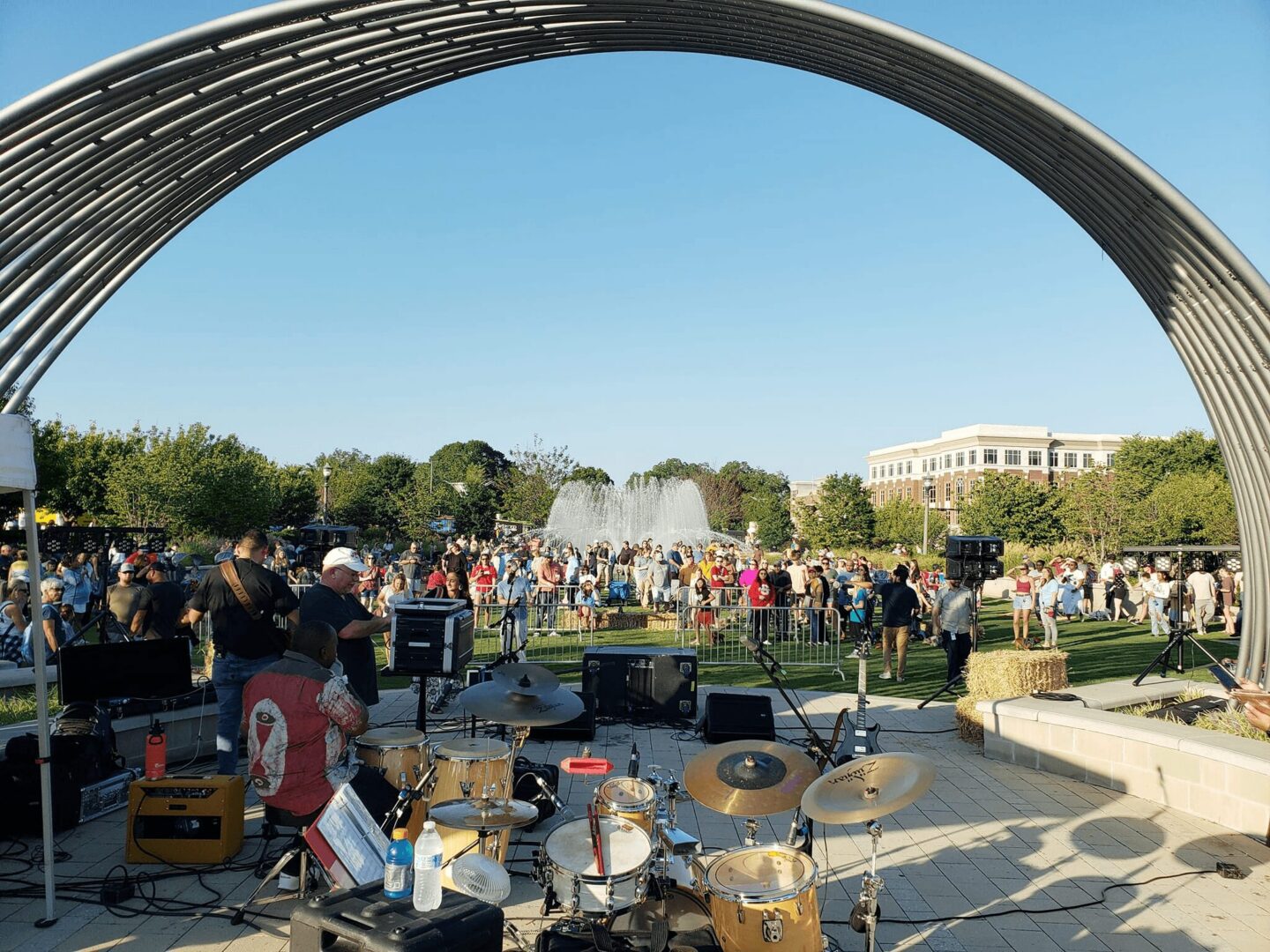 Outdoor concert with crowd and fountain backdrop.